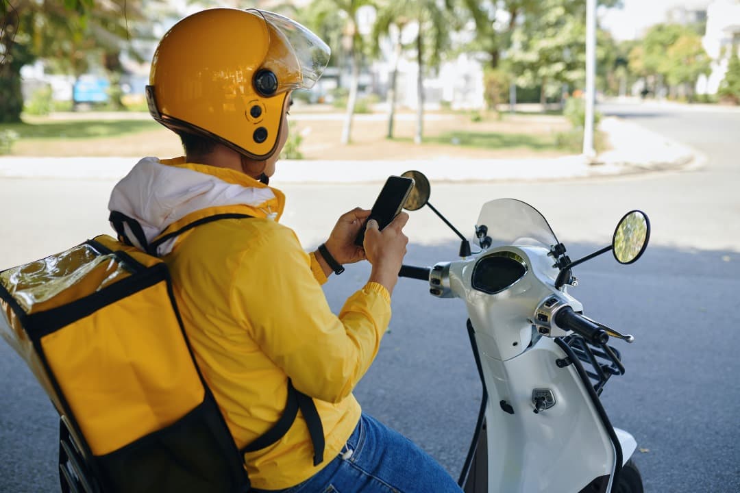 Delivery rider checking a phone beside a scooter
